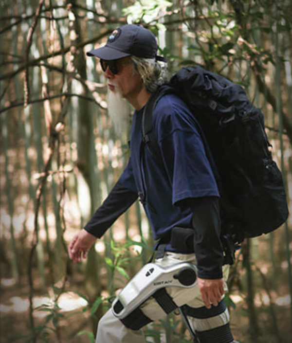 Man hiking in forest wearing outdoor gear and robotic exoskeleton with backpack